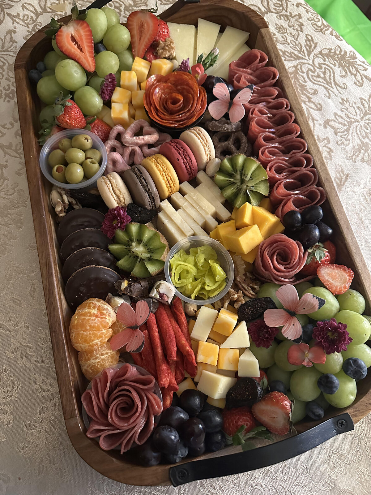 Abundant oval charcuterie board with salami roses, fresh fruit, cheeses, and macarons